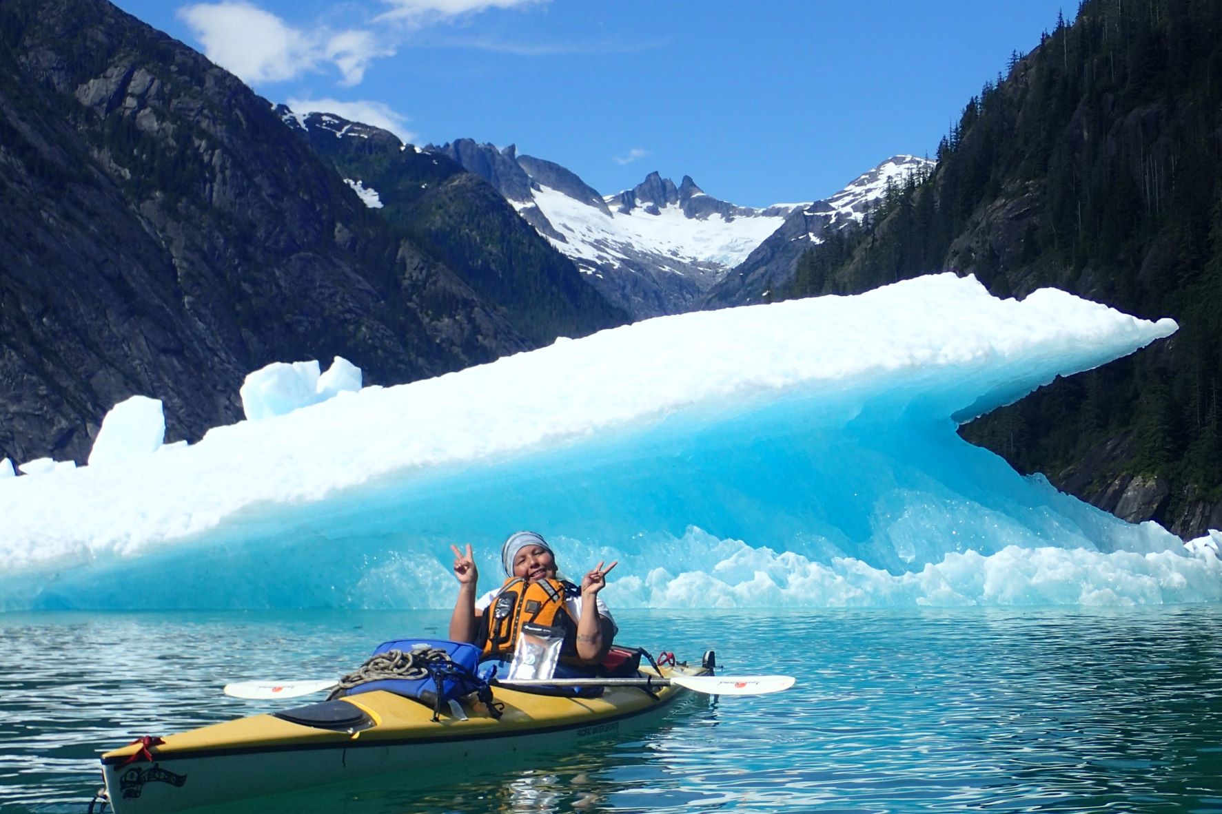 Stacey Skan smiles in a kayak in front of an iceberg.