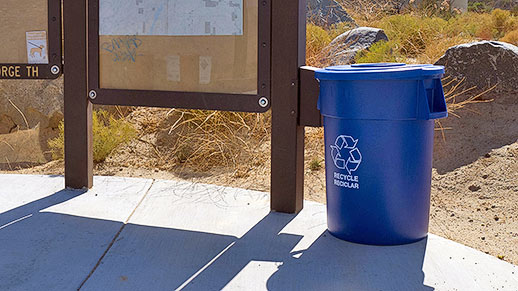 Plastic recyling can placed outdoors adjacent to signs.