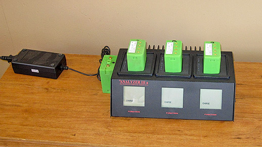 A square electrical device with three green batteries inserted in it.