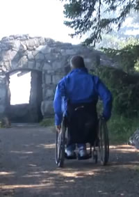 photo of man in wheelchair approaching stone arch on Whispering Spruce Trail