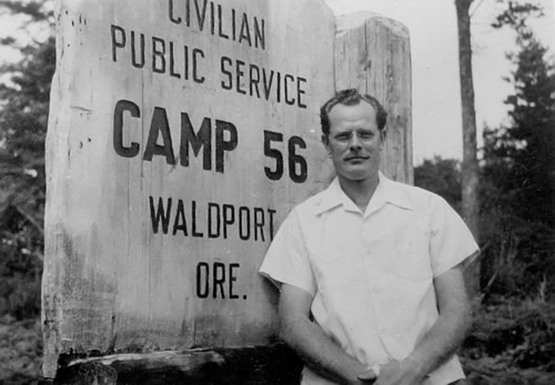 man standing by the wooden sign for Camp 056 at Camp Angell