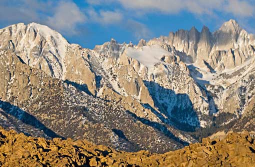 Snow-capped mountains casting shadows in a rocky, rugged wilderness area.