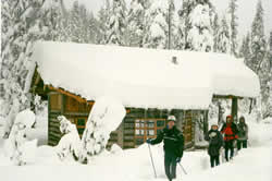Maiden Peak Shelter with deep snow on roof and skiers along side