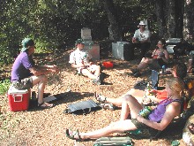 A group of campers talks in a circle in their forested camp.