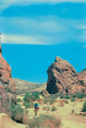 a hiker walks through a desert with big boulders and a blue sky