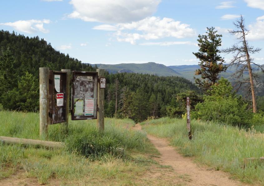 Image of the Coulson Gulch informational kiosk and trail with a meadow in the background