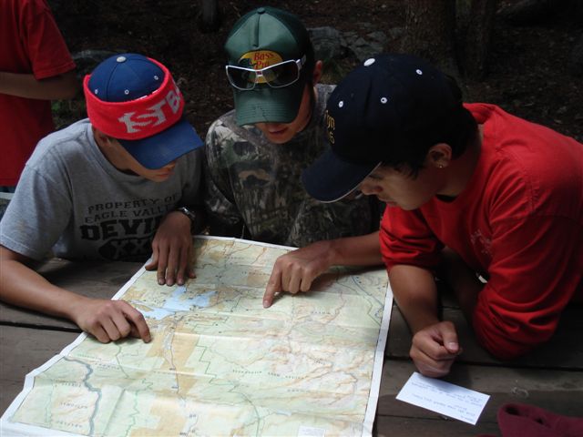 Three youth wearing baseball caps look at a map.