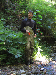 Dr. Daniel Cenderelli wearing fishing waders, standing on a bed of river rock.