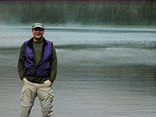 Dr. David H. Levinson standing in front of a large body of water, and a foggy forest of trees in the far background.