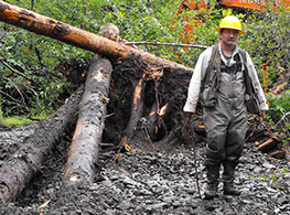 Image of Robert Gubernick standing in front of a mishmash of trees partially buried in the mud and rocks.