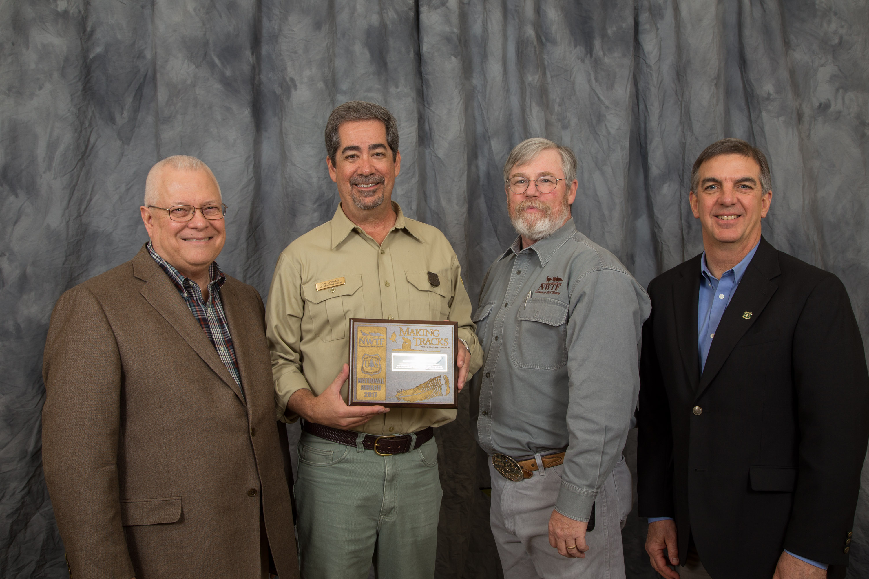 Photograph of Southwestern Regional Forester, Cal Joyner accepting the award for Ian Fox.  To left is NWTF's Gene Miller; to right is NWTFs Scott Lerich, and Making Tracks Steering Committee Member/Regional Wildlife Program Leader, Brian Dykstra. 