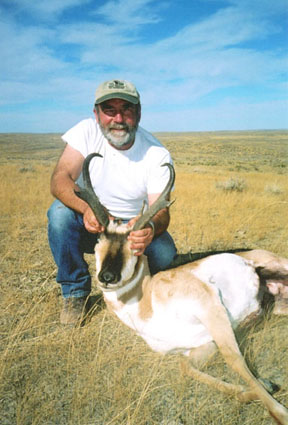 Photograph: USFS Region 1 Wildlife biologist, Skip Kowalski kneeling with an antelope out on a grassland with blue skies.