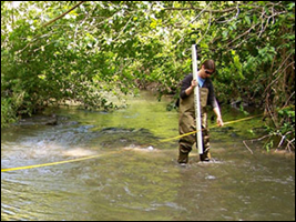 tech taking stream measurements wear waders in a stream