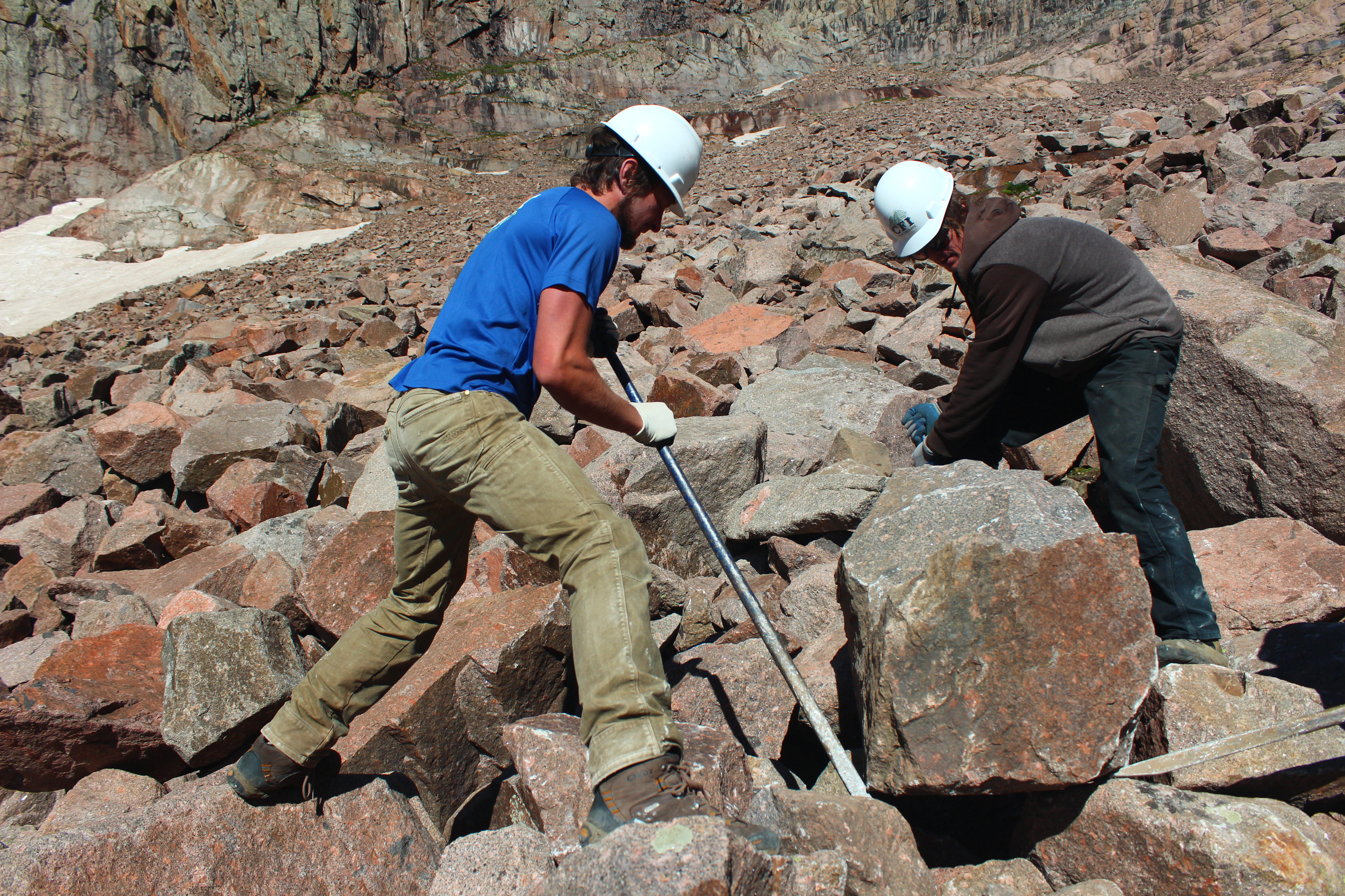 Image of trail workers using a pry bar to move a boulder.