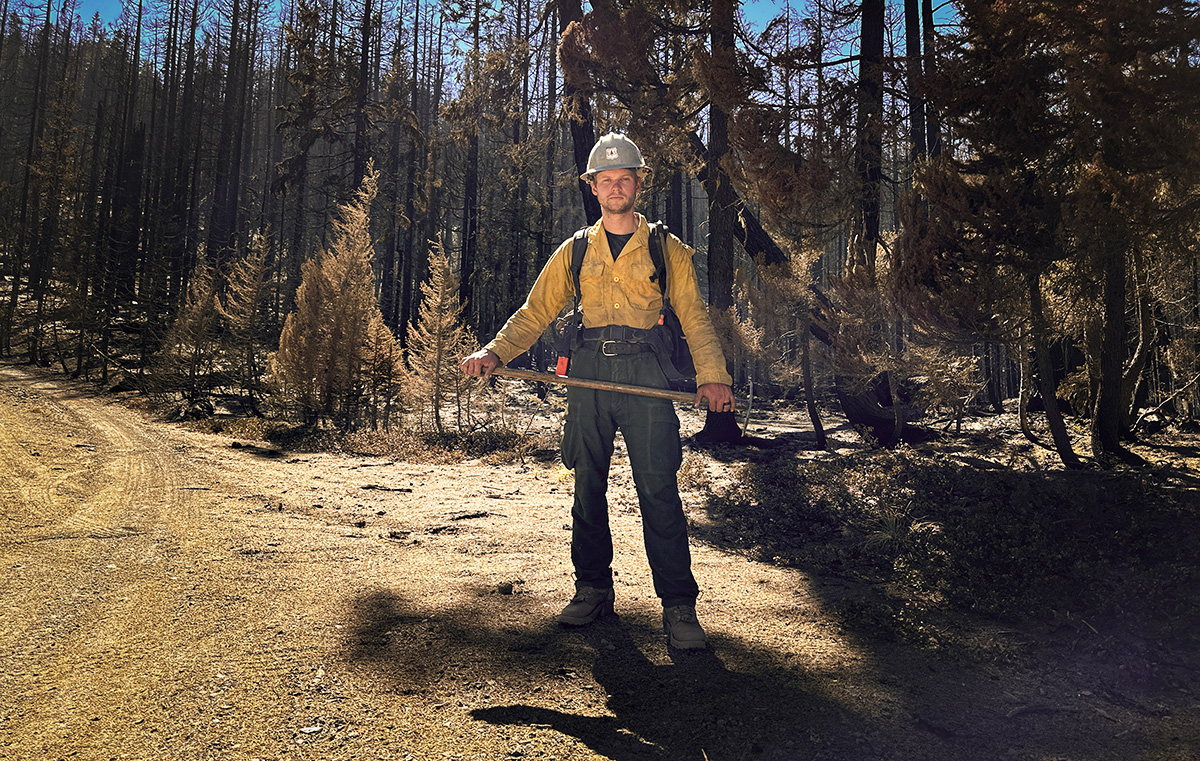 Forest Service wildland firefighter Ben McLane standing next to a dirt road holding a tool.
