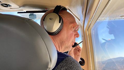 A person in sitting in a flying aircraft looking out the right window while appearing to talk in the microphone of a headset.