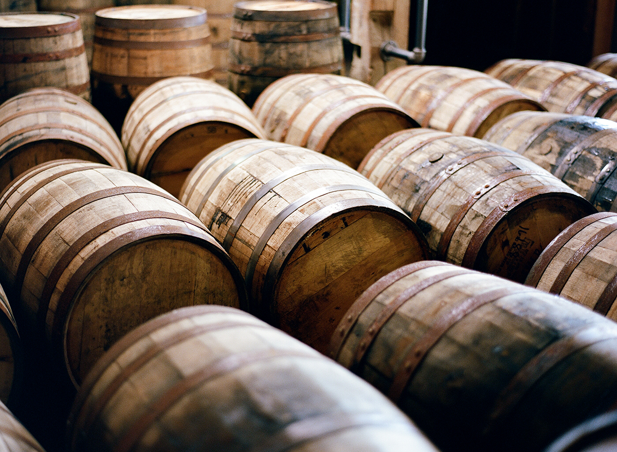 Image shows a series of oak barrels that had been used for bourbon-making lying on their side in rows.