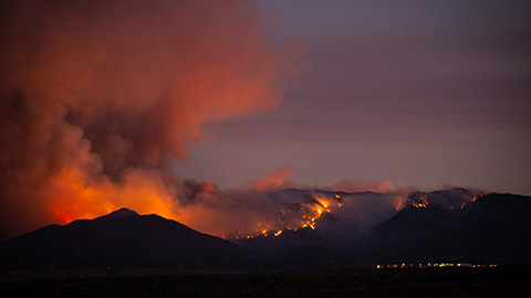 Wildfire burning in mountains at night above a community