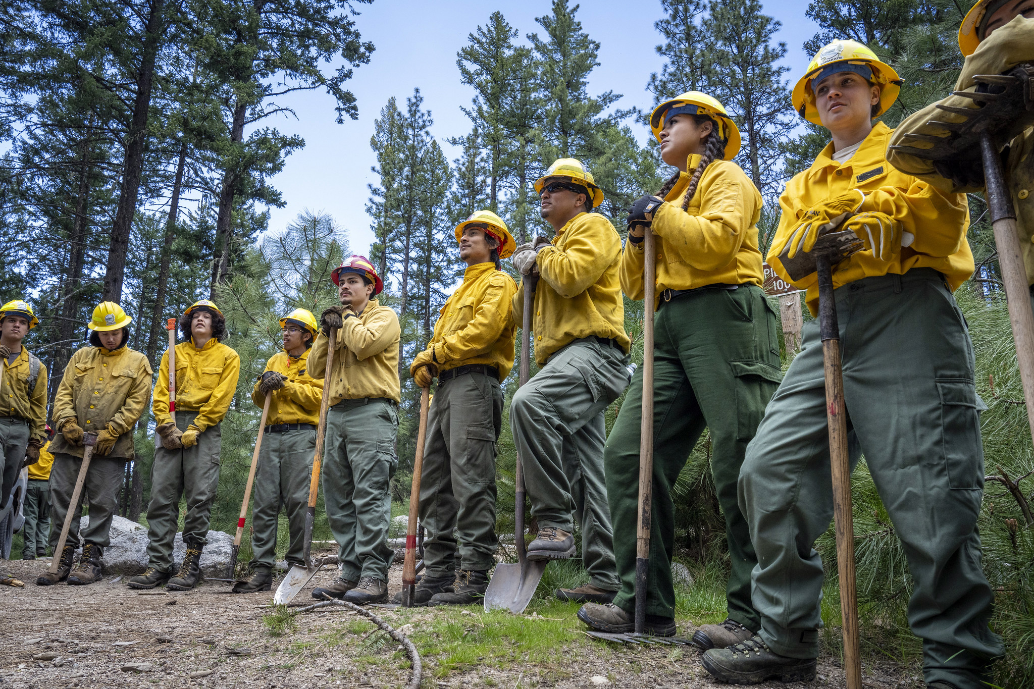 Inter-tribal youth standing in a half circle wearing wildland fire fighter safety closing and hold tools.