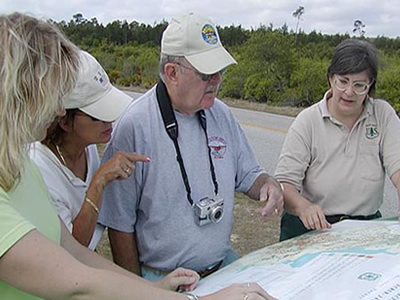 A group of 4 individuals looking at a map on the hood of a vehicle.