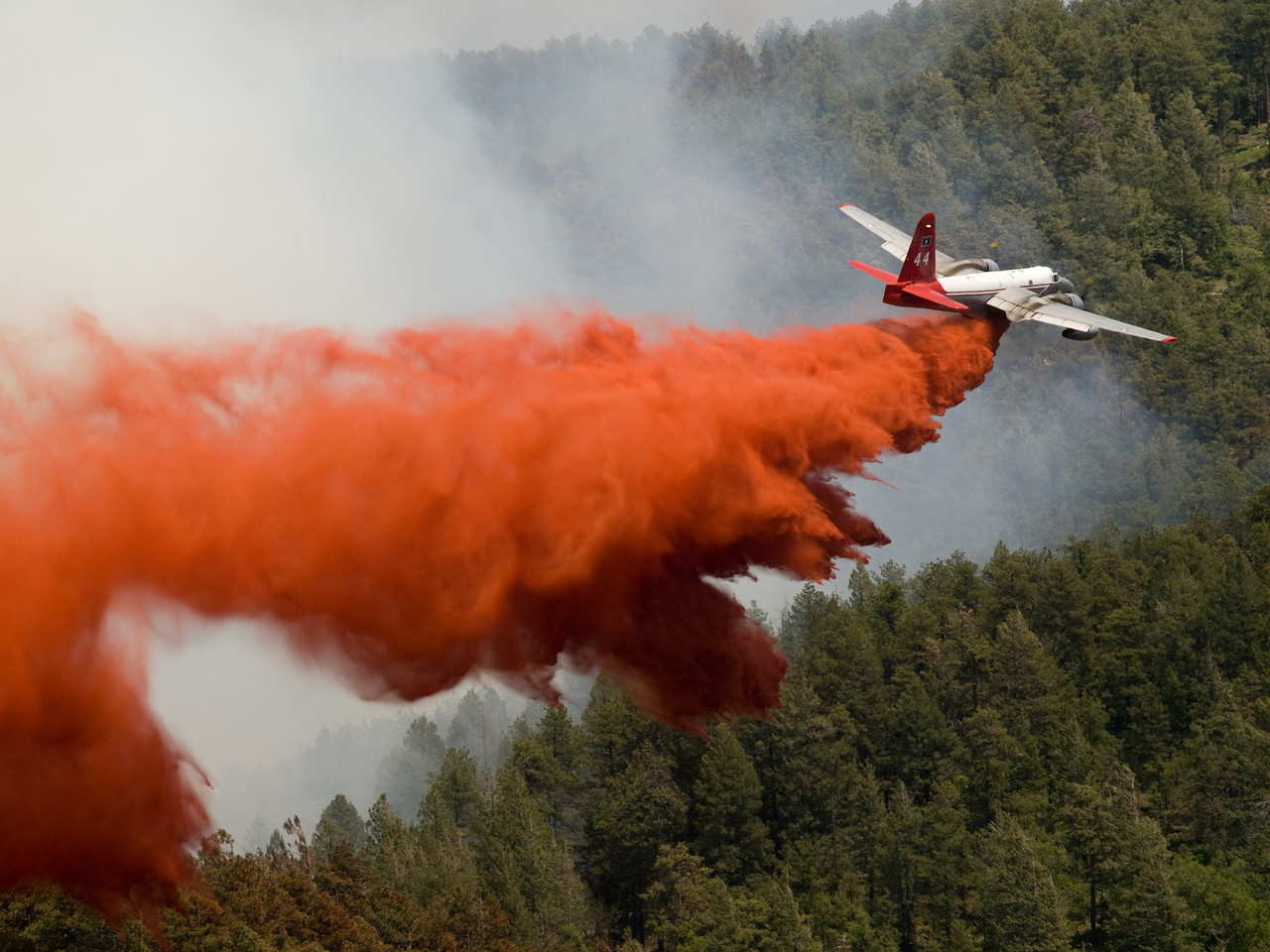 A large airtanker aircraft dropping red fire retardand in the path of a forest fire.