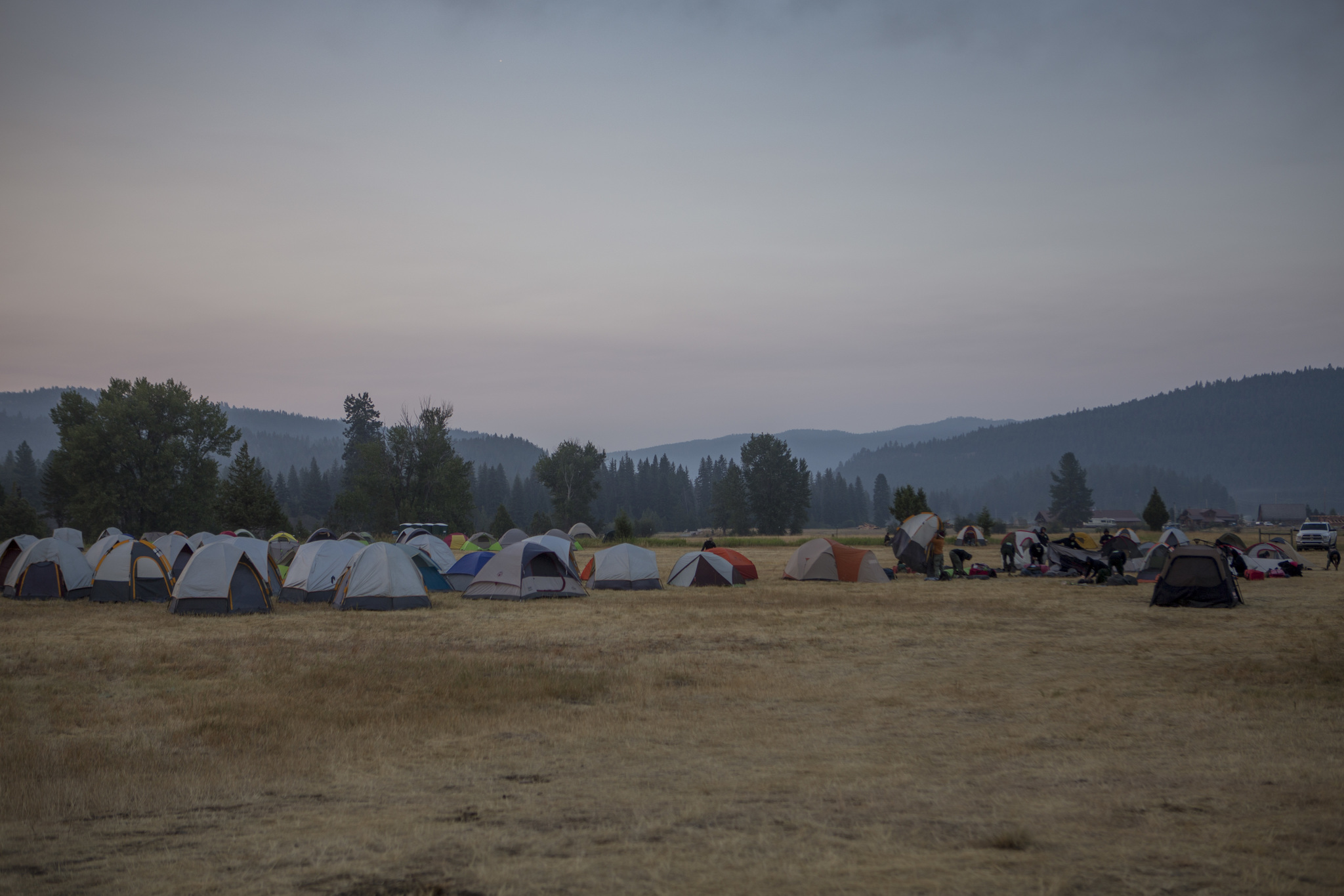 A fire incident basecamps with multiple tents set up in an open field under a smokey sky.
