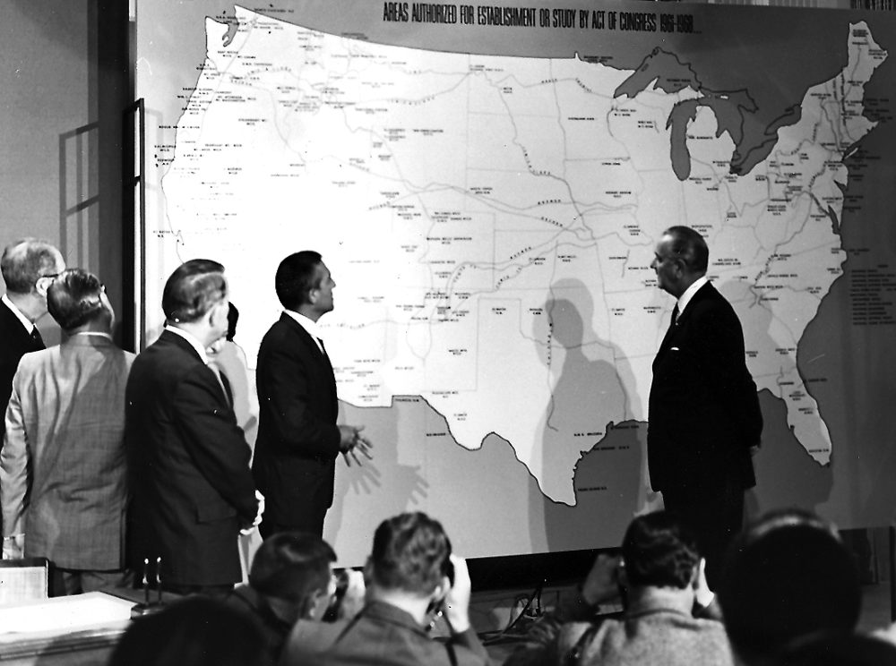 A black and white picture of President Johnson discussing a map of the proposed National Trails System