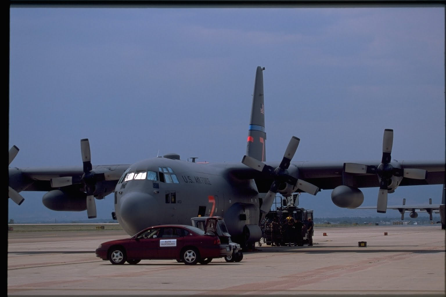 Modular Airborne Fire Fighting Systems (MAFFS) aircraft at an airport. A car and small vehicle are parked in front of the aircraft.