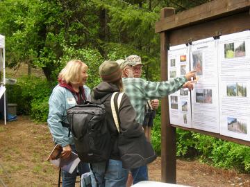 People looking at a visitor bulletin board at a trail head.