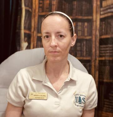 Meredith Hollowell seated in a library. Wearing uniform polo shirt and name tag.