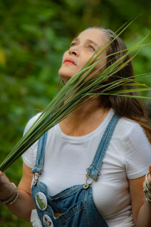 A picture of Azul Aguayo holding several strands of very tall grasses as she looks towards the sky.