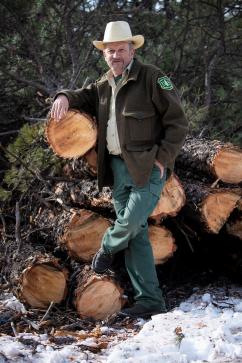 Picture of Tom Dauenhauer wearing Forest Service uniform and leaning against logs.