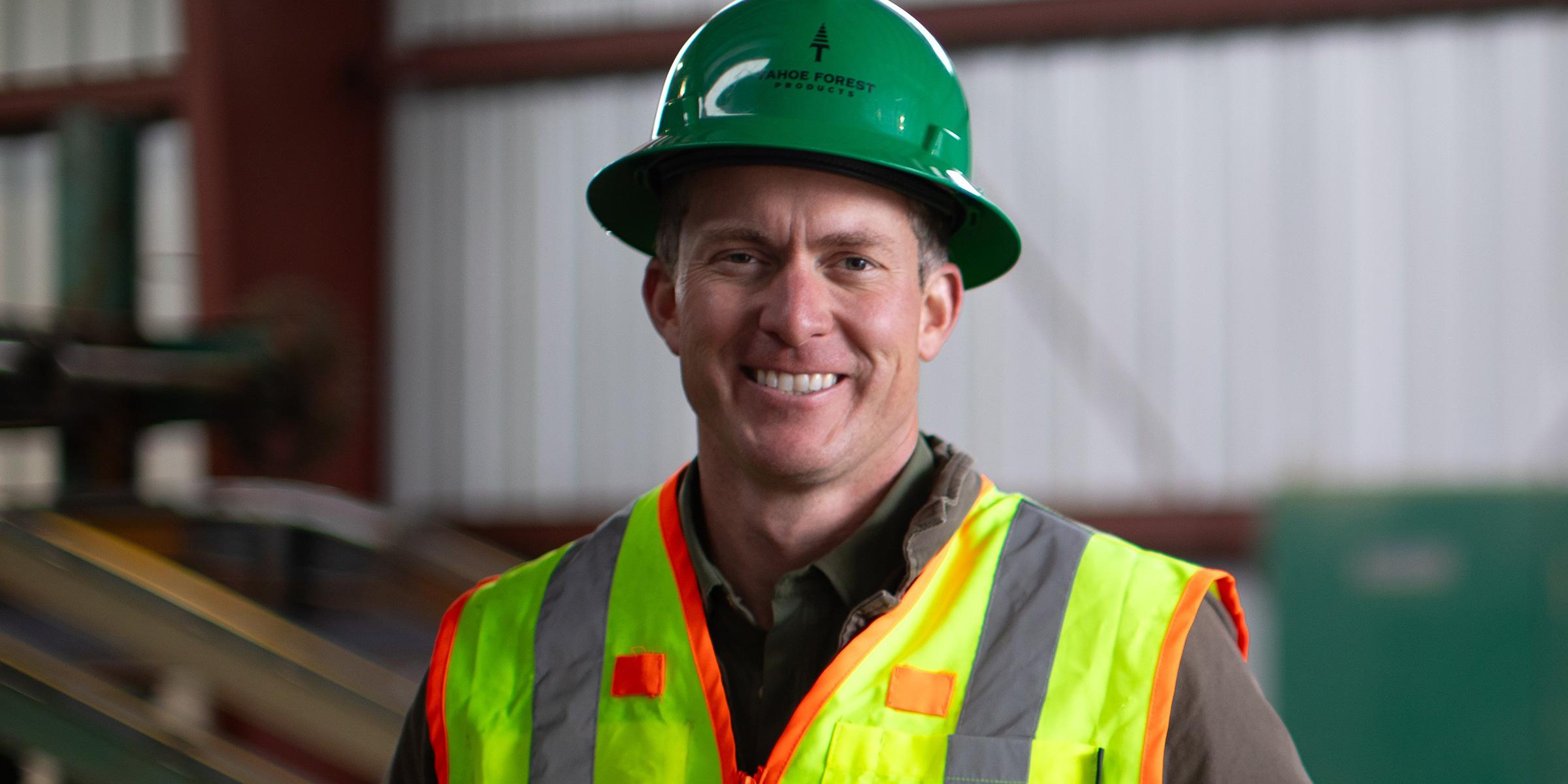 Man in green hardhat and safety vest standing near a saw mill