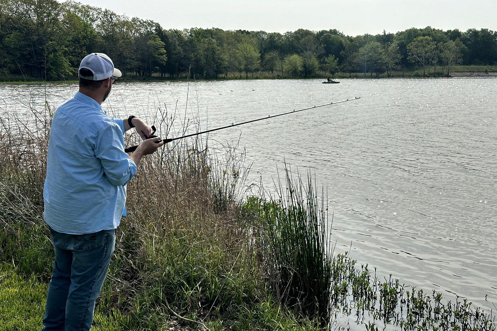 A person fishing on a lake from the banks of a lake.
