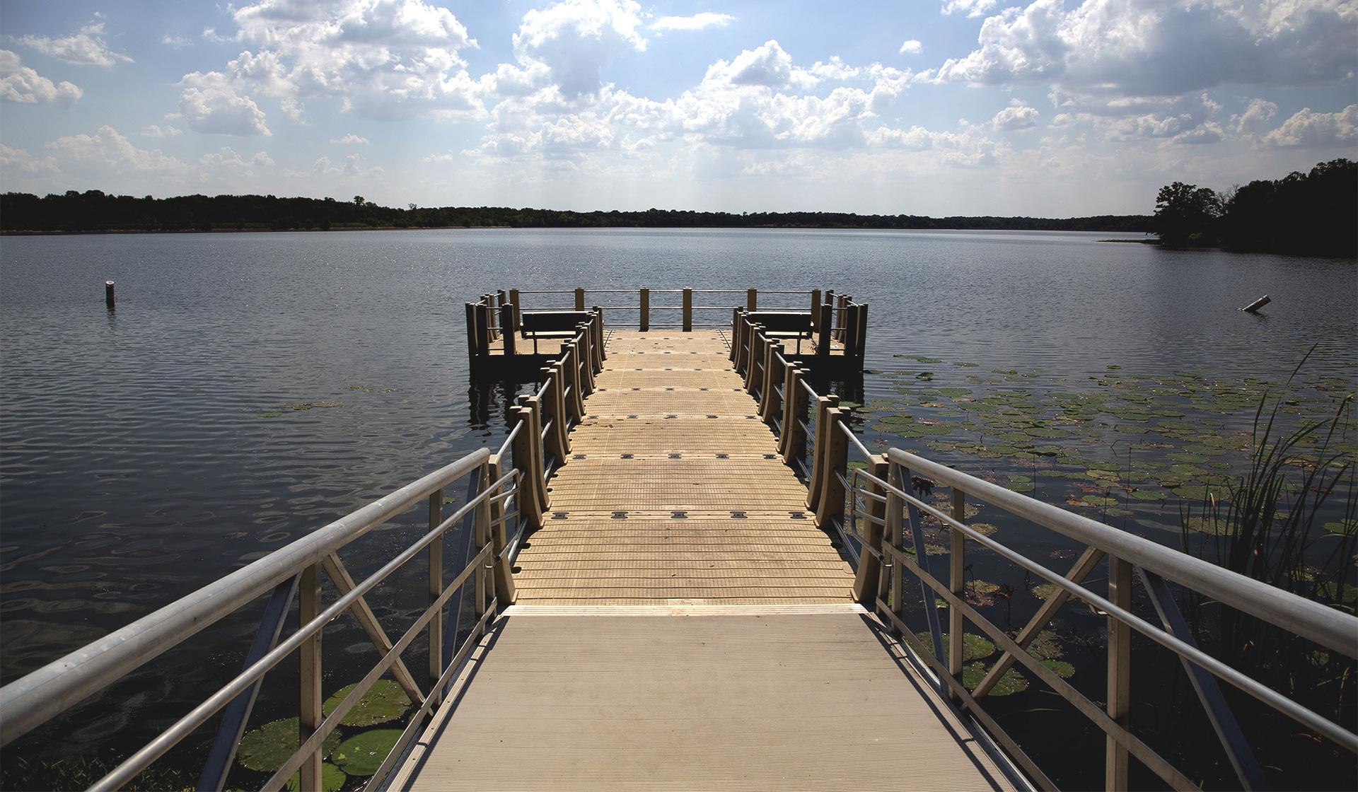 Image shows a wooden pier extending out into a blue lake with clear skies overhead.