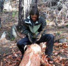 Photo of Trapper Creek Job Corps student Chris Dickenson using hand tools to peel logs
