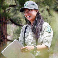 A person wearing a USDA Forest Service shirt and hat holding a clipboard and laughing.