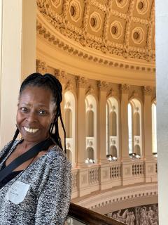 Joyce Davis leaning against a railing on an upper level of the U.S. Capitol with the dome visible just above her.