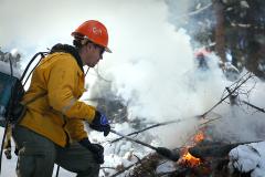 Firefighter, Stewart Parsons, using a propane torch to burn a pile of limb debris buried under the snow.