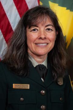 Portrait: Michiko Martin in formal Forest Service uniform in front of American and Forest Service flags.
