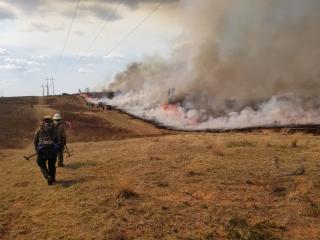 Firefighter in full gear walking next to a prescribed burn fire. Smoke is billowing