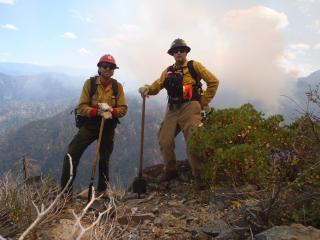 A picture of two wildland firefighters on top of a mountain area wearing their wildland firefighting gear and equipment.