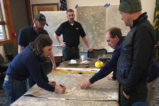 A picture of five forest managers looking down at a map and planning their next actions in a forest area.