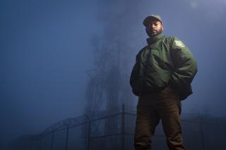 Uniformed employee standing on foggy mountain top near radio tower.