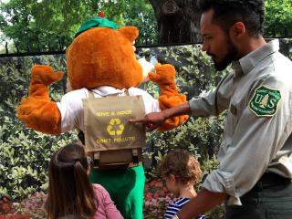 Education Specialist points at Woodsy Owl's backpack for two children. The backpack reads with Woodsy's slogan: Give a Hoot, Don't Pollute.