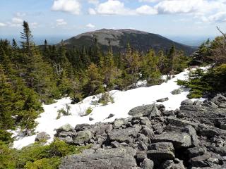 Snow still partially covers a hillside in western Maine. Mount Abraham is visible in the background.