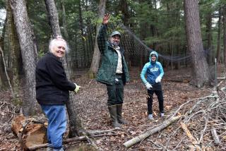 Three people in forest hold up fencing to install around an area where trees will be planted.