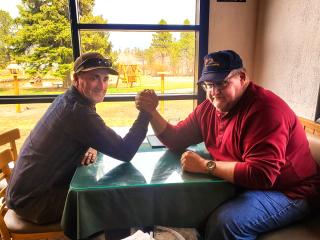 Image of Forest Service employee and Army veteran, Louis Haynes arm wrestling with Flaming Gorge recreation program manager Kevin Clegg, indoors, at a table, next to a window.