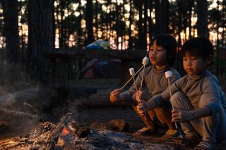 Two little boys enjoying s’mores by a campfire.
