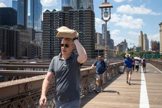 A man shields his head from the sun as he walks across the Brooklyn Bridge on a hot summer day in New York City.